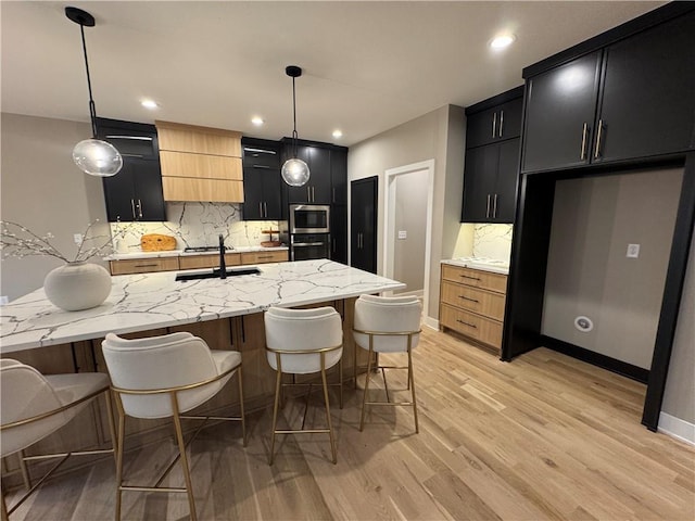 kitchen featuring decorative backsplash, dark cabinetry, light wood-type flooring, and appliances with stainless steel finishes