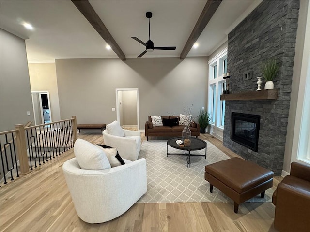 living area with a stone fireplace, beam ceiling, a ceiling fan, and light wood finished floors