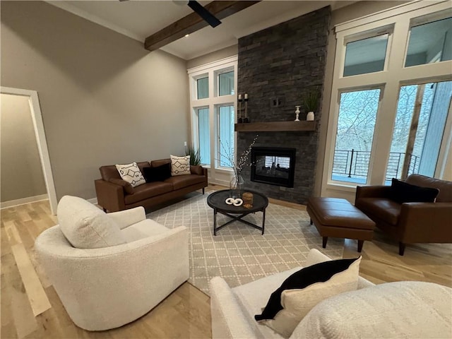 living room with beam ceiling, a stone fireplace, light wood finished floors, and a high ceiling