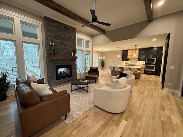 living area featuring beam ceiling, light wood-style flooring, a ceiling fan, and baseboards