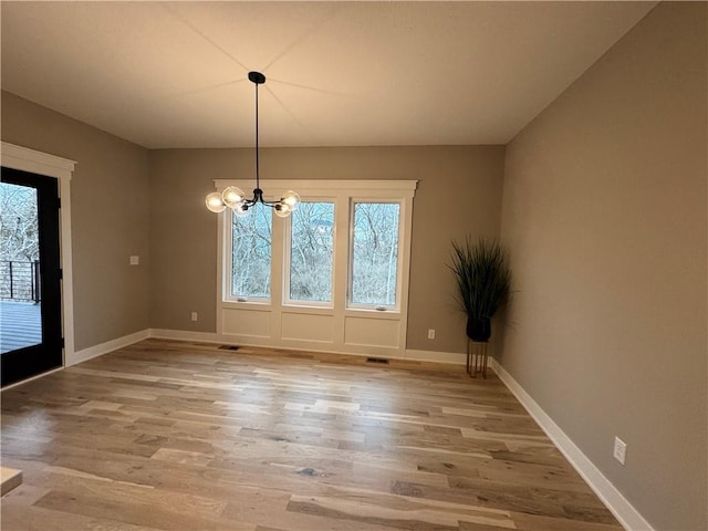 unfurnished dining area featuring plenty of natural light, light wood-style floors, and a chandelier