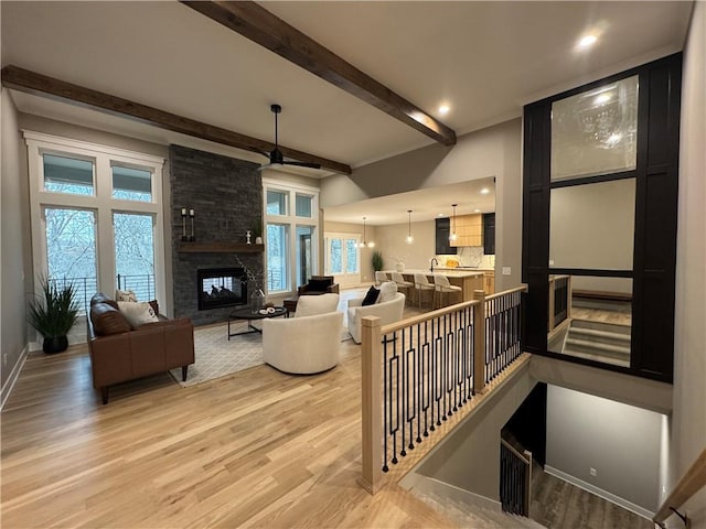 living area with beamed ceiling, baseboards, a stone fireplace, and light wood-style flooring