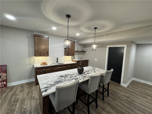 kitchen with a sink, dark wood-type flooring, tasteful backsplash, and a breakfast bar area