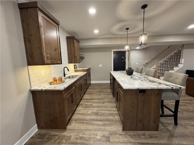 kitchen with a center island, decorative backsplash, a kitchen breakfast bar, wood finished floors, and a sink