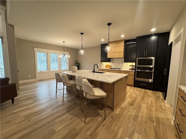 kitchen featuring light wood finished floors, a kitchen bar, appliances with stainless steel finishes, dark cabinetry, and a sink