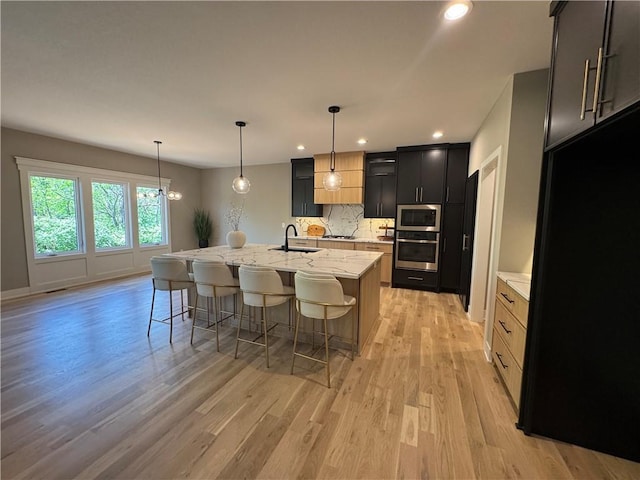 kitchen featuring a breakfast bar area, a sink, light wood-style flooring, backsplash, and stainless steel appliances