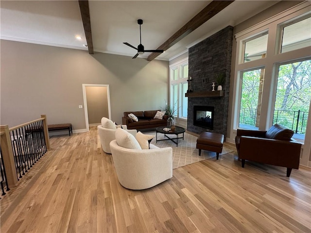 living area with ceiling fan, a large fireplace, beam ceiling, baseboards, and light wood-style flooring