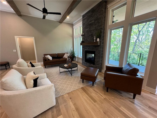 living room featuring beam ceiling, a stone fireplace, baseboards, a ceiling fan, and light wood-style flooring