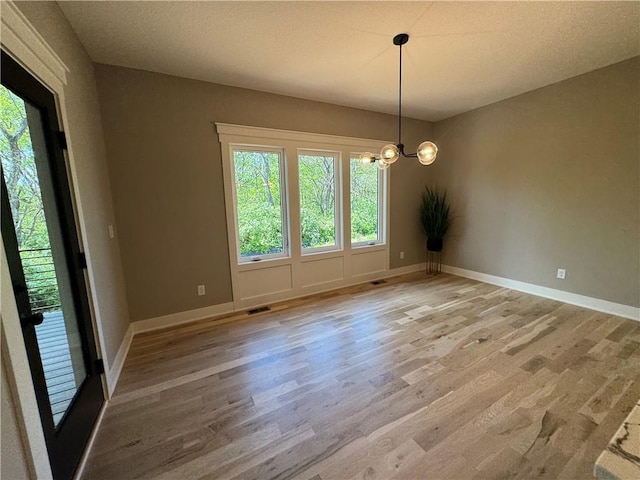 unfurnished dining area with a chandelier, visible vents, a healthy amount of sunlight, and wood finished floors