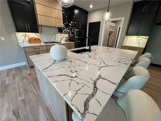 kitchen with dark cabinets, stainless steel microwave, a sink, and light wood-style floors
