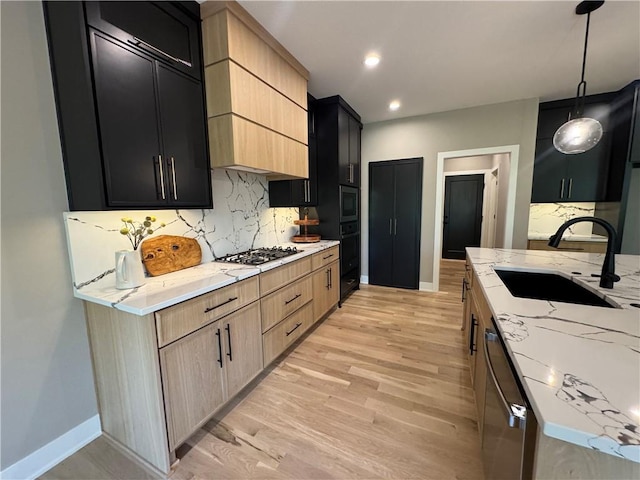 kitchen with light stone countertops, light wood-style floors, a sink, appliances with stainless steel finishes, and backsplash