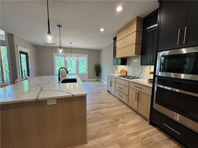 kitchen featuring a sink, light wood finished floors, a kitchen island with sink, and stainless steel appliances