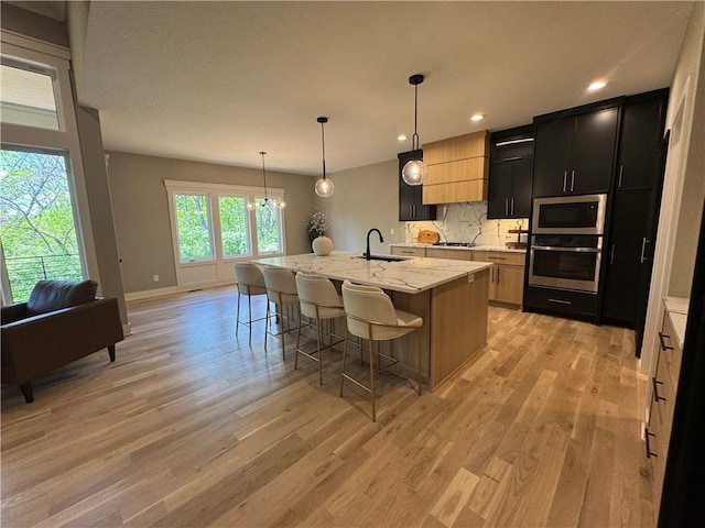 kitchen with a kitchen breakfast bar, appliances with stainless steel finishes, a sink, dark cabinets, and light wood-style flooring