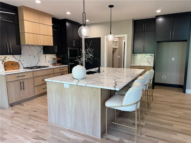 kitchen with backsplash, a sink, stainless steel appliances, light wood-style flooring, and an island with sink