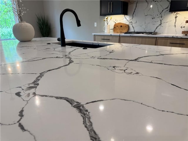 room details with light stone counters, a sink, white gas stovetop, and dark cabinets