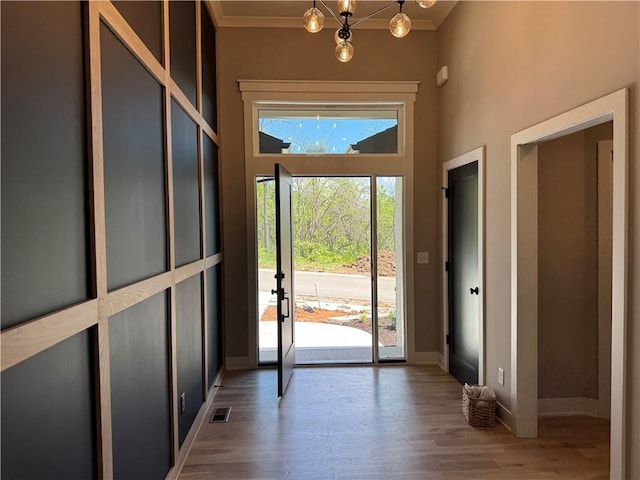doorway with baseboards, a notable chandelier, wood finished floors, and visible vents