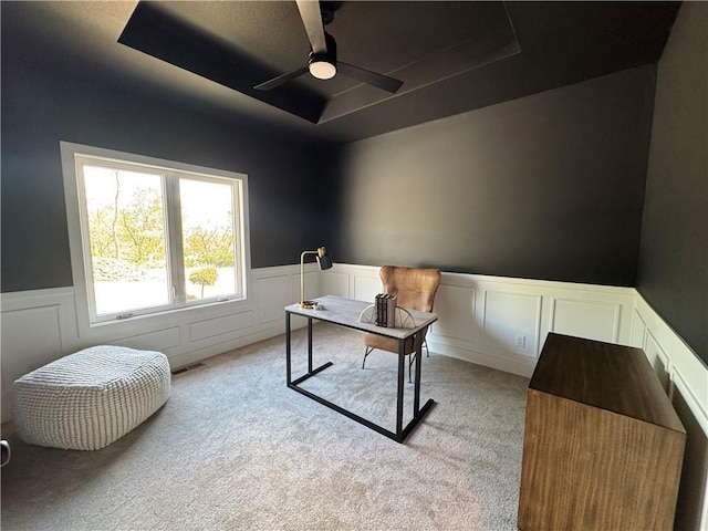 office with visible vents, light carpet, ceiling fan, a wainscoted wall, and a tray ceiling