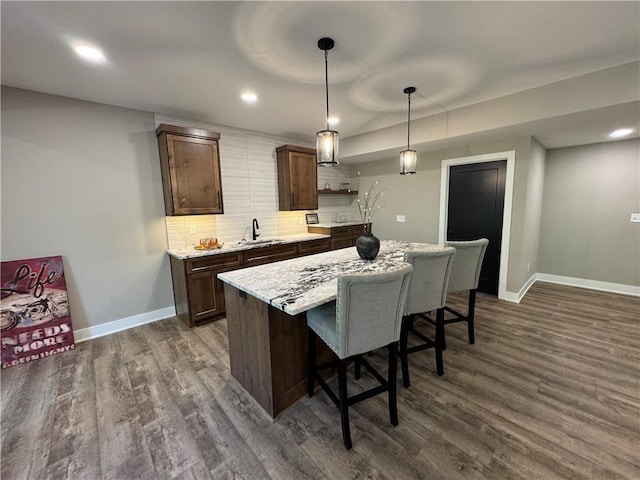 kitchen with open shelves, a breakfast bar, a sink, dark wood-type flooring, and a kitchen island