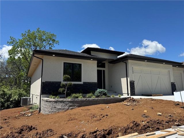 prairie-style house with a garage, stucco siding, central AC, and stone siding