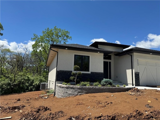 prairie-style home featuring an attached garage, cooling unit, stone siding, and stucco siding