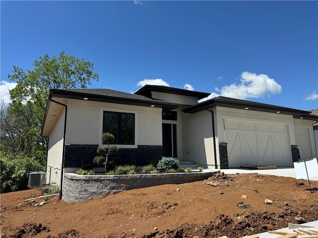 prairie-style home featuring stucco siding, a garage, central air condition unit, and stone siding