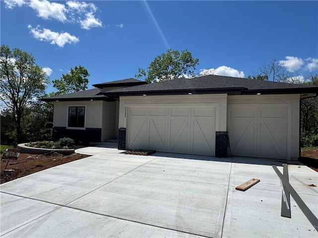 prairie-style home featuring a garage, stucco siding, driveway, and a shingled roof