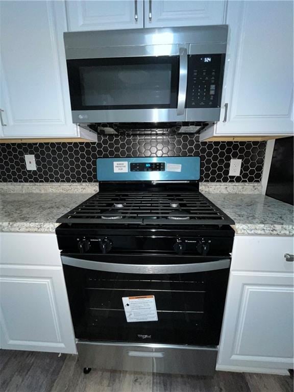 kitchen featuring stainless steel microwave, backsplash, gas range oven, and white cabinetry