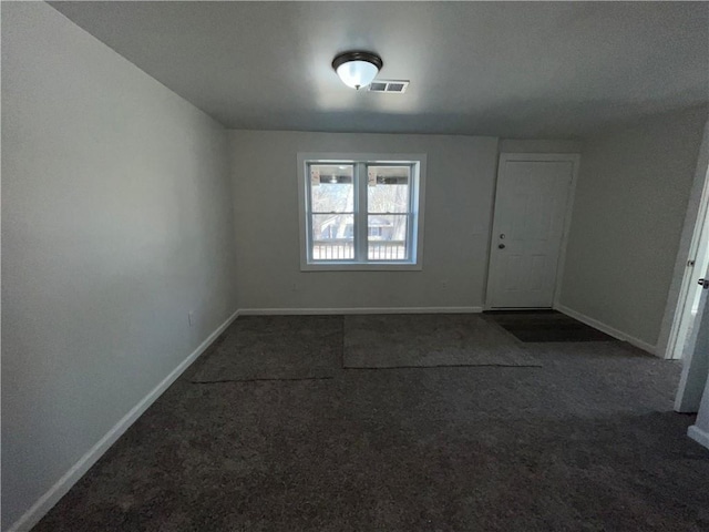 spare room featuring baseboards, visible vents, and dark carpet