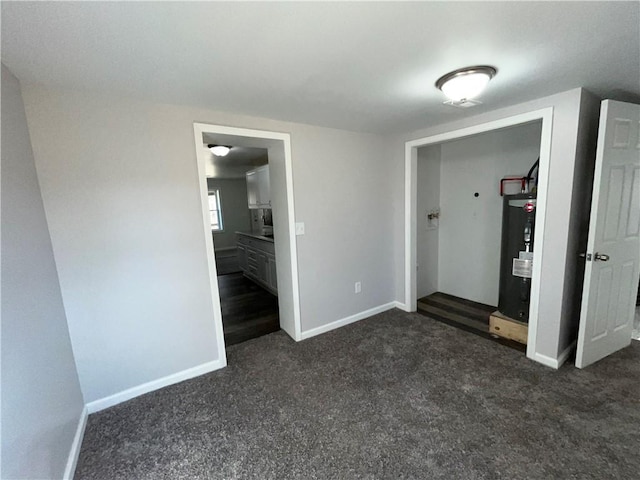 unfurnished bedroom with dark colored carpet, baseboards, ensuite bath, and water heater