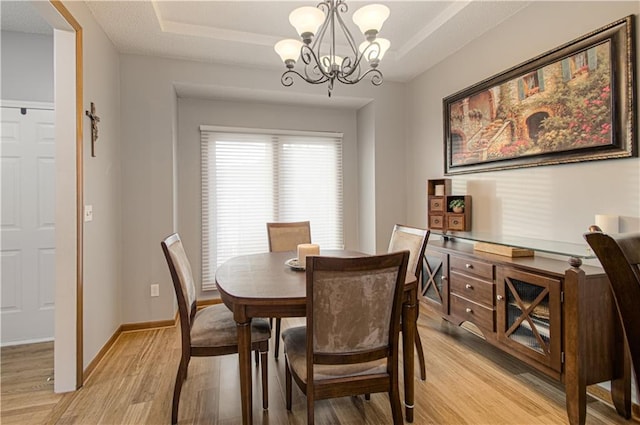 dining space featuring a tray ceiling, a notable chandelier, and light wood-style floors