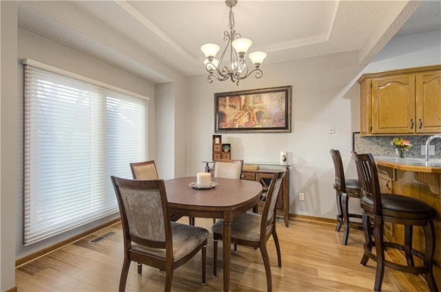 dining space featuring visible vents, baseboards, an inviting chandelier, light wood-style floors, and a raised ceiling