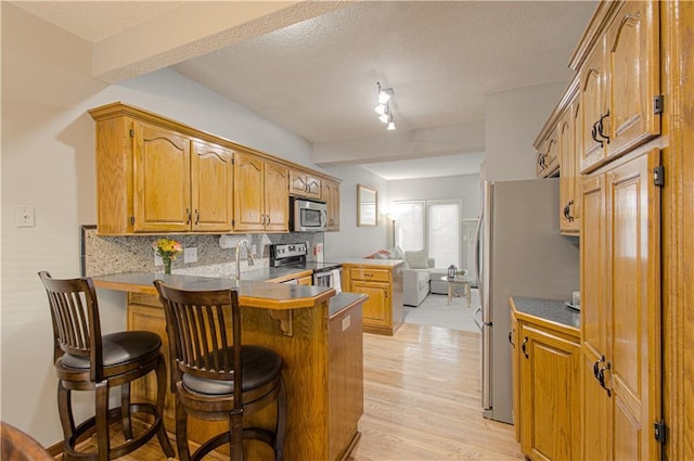 kitchen featuring a peninsula, stainless steel appliances, decorative backsplash, light wood-style floors, and a kitchen bar