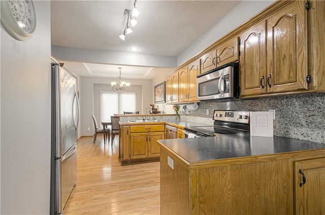 kitchen featuring light wood-type flooring, appliances with stainless steel finishes, a peninsula, a raised ceiling, and a sink