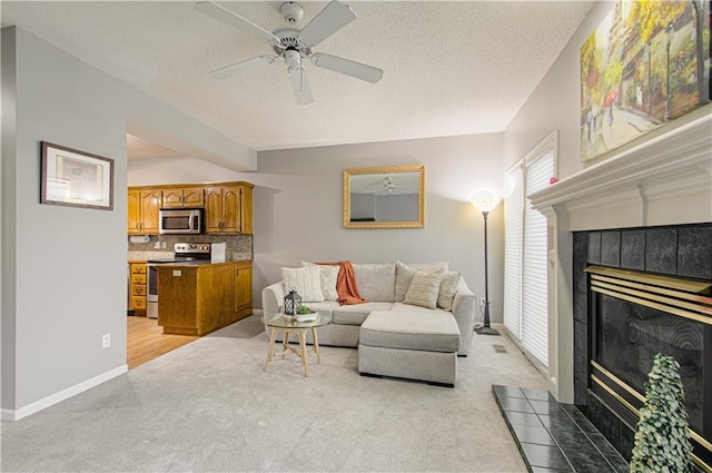 living room with a ceiling fan, light carpet, a textured ceiling, and a tiled fireplace