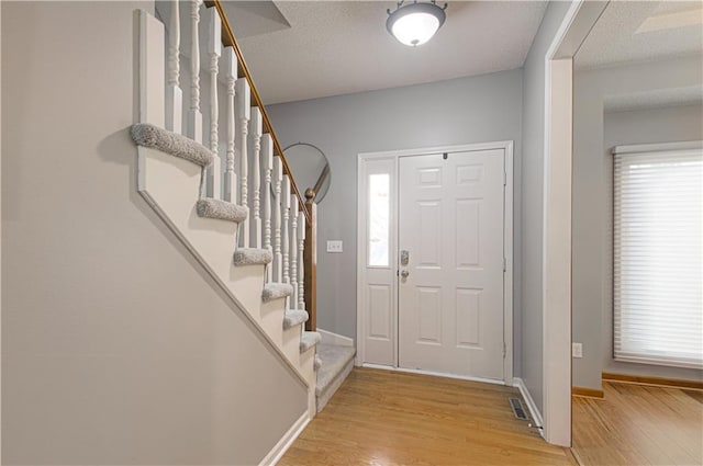 foyer entrance with light wood finished floors, stairway, a textured ceiling, and baseboards