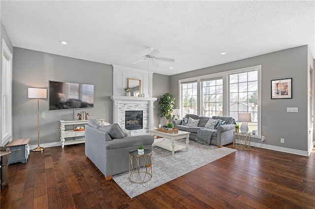 living area with a glass covered fireplace, baseboards, dark wood-type flooring, and ceiling fan