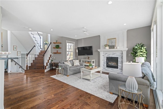 living area with a ceiling fan, a glass covered fireplace, wood finished floors, recessed lighting, and stairway