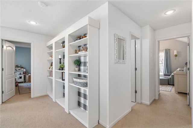 hallway featuring a textured ceiling, recessed lighting, baseboards, and light carpet