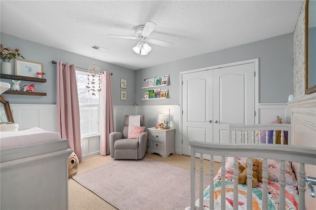 carpeted bedroom with visible vents, wainscoting, a textured ceiling, and a ceiling fan