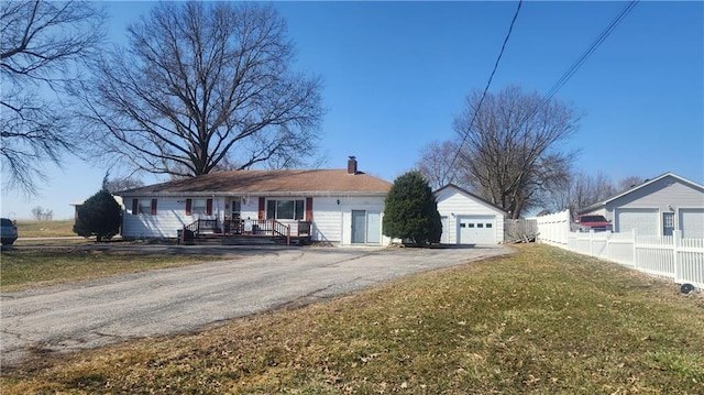 view of front facade with driveway, fence, an outdoor structure, a front yard, and a chimney