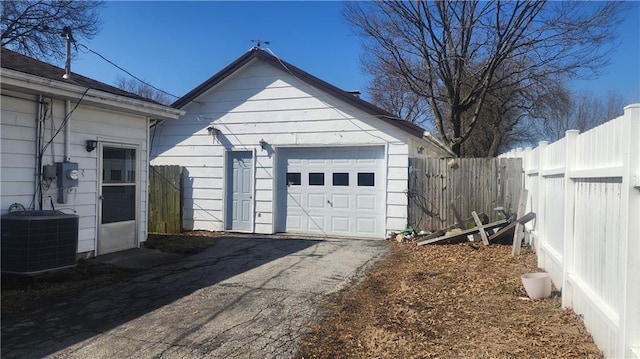 detached garage featuring aphalt driveway, fence, and central AC