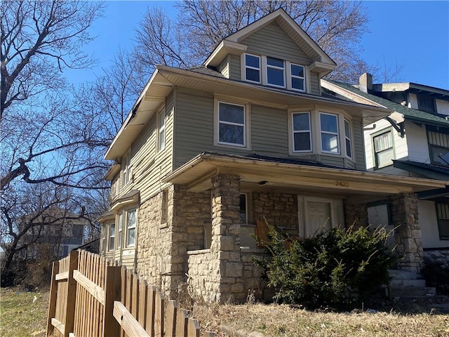 view of home's exterior with stone siding, covered porch, and fence