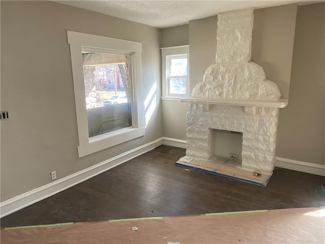 unfurnished living room with baseboards, a textured ceiling, a stone fireplace, and wood finished floors