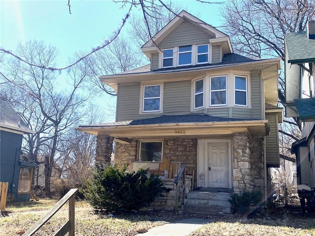 traditional style home featuring covered porch, stone siding, and a shingled roof