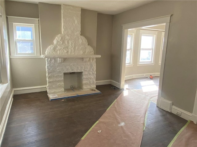 unfurnished living room with a wealth of natural light, baseboards, a stone fireplace, and dark wood-style floors