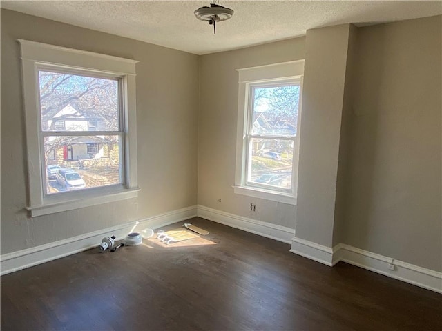 empty room featuring baseboards, a textured ceiling, and dark wood-style flooring