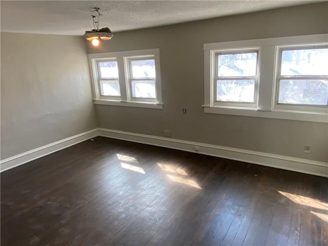 empty room with a healthy amount of sunlight, baseboards, dark wood-style flooring, and a textured ceiling