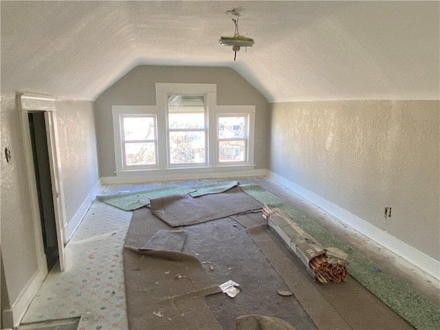 bonus room with baseboards, lofted ceiling, a textured ceiling, and a textured wall