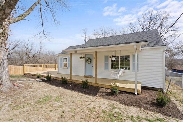 view of front of home featuring roof with shingles, covered porch, and fence