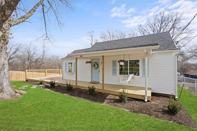 view of front facade featuring a front lawn, fence, covered porch, and a shingled roof